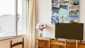 A room with a wooden dining table, chairs, a TV on a wooden stand, a vase with flowers, and a wall with nautical-themed pictures. - Apartment 'Mediterranean View 3-1' close to the Beach with Terrace & Wi-Fi (Llançà)