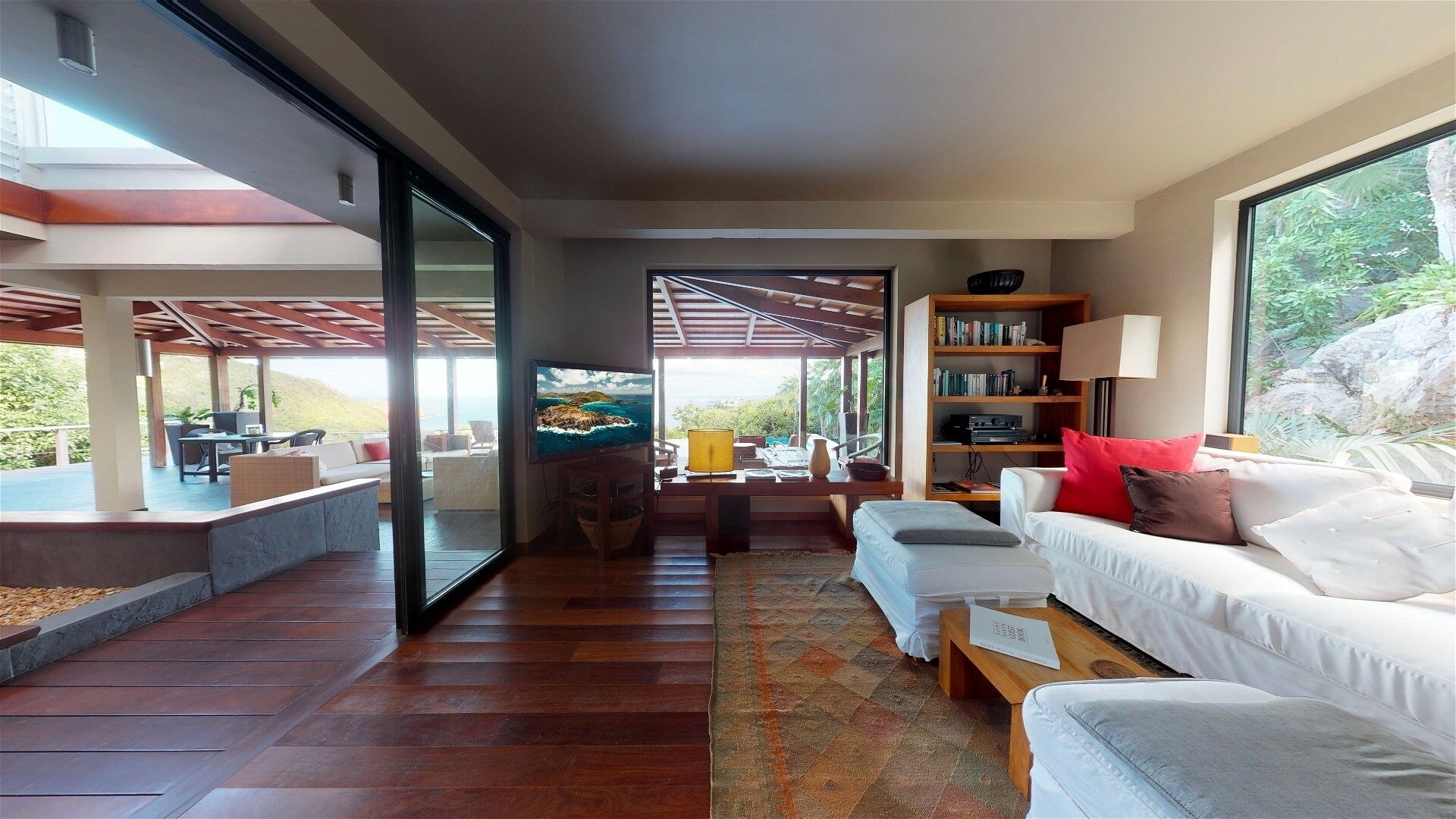 A modern living room with a large TV, a bookshelf, and a view of the outdoors.