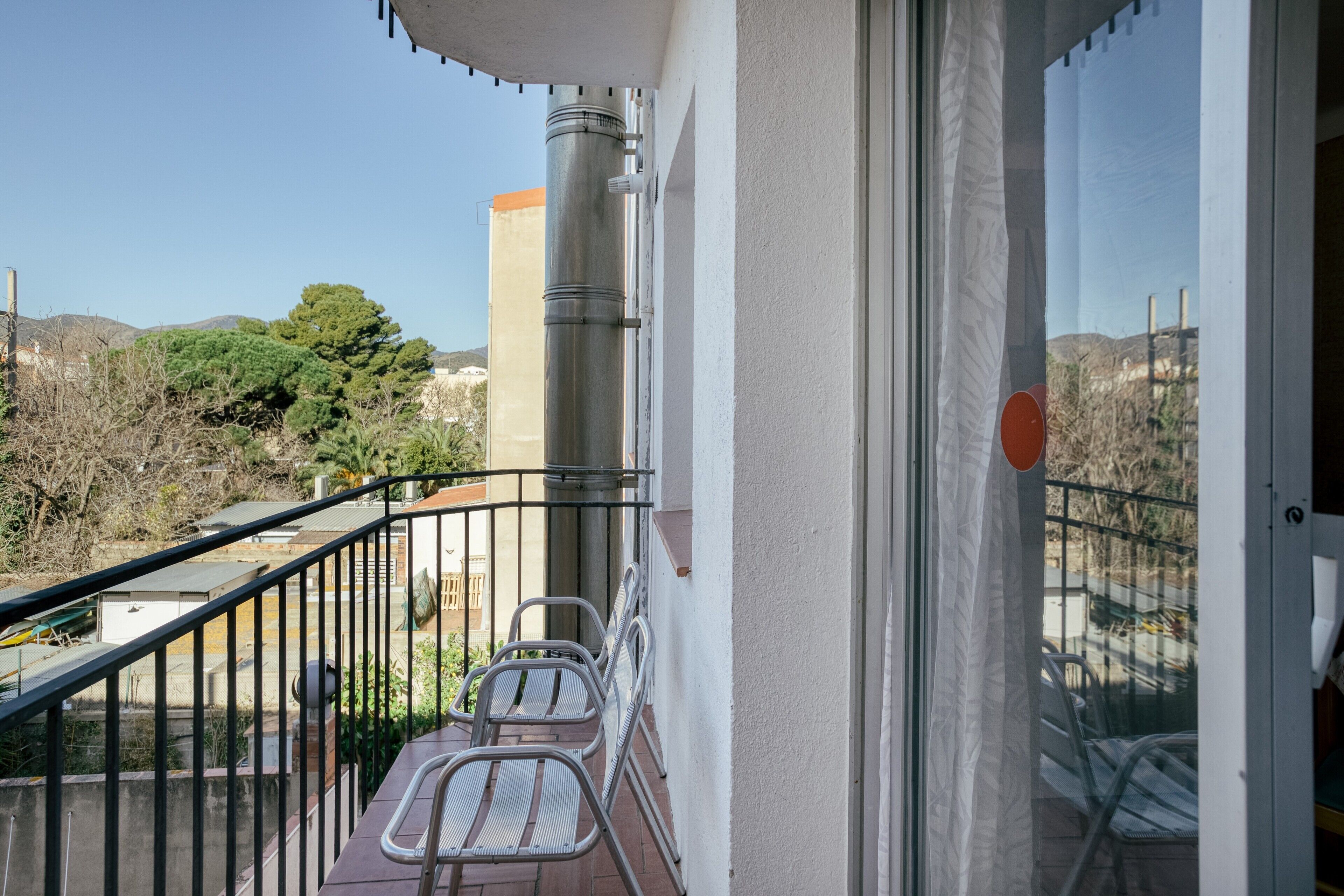 A balcony with metal railings, a few chairs, and a view of the surrounding landscape.