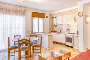 A compact kitchen with white cabinets, a stove, and a sink. There is a dining area with a table and chairs.
