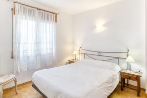 A bedroom with a bed, two bedside tables with lamps, a chair, and a window with sheer curtains.
