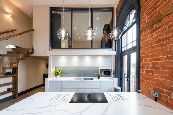 A modern kitchen with a marble countertop, stainless steel appliances, and pendant lighting.
