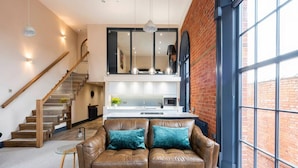 A modern living room with a brown leather sofa, a glass coffee table, and a staircase leading to an upper level. - Apartment 2 The Old Chapel apartments, in the heart of Sherwood Forest (Edwinstowe, Nottinghamshire)