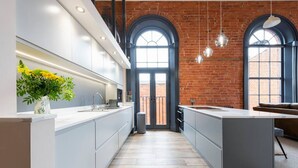 A modern kitchen with white cabinetry, a central island, and a brick wall. - Apartment 2 The Old Chapel apartments, in the heart of Sherwood Forest (Edwinstowe, Nottinghamshire)