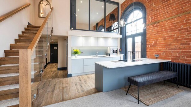 A modern kitchen with a large island, a wooden staircase, and a brick wall. - Apartment 2 The Old Chapel apartments, in the heart of Sherwood Forest (Edwinstowe, Nottinghamshire)