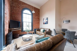 A living room with a brick wall, a large window, a leather sofa, a coffee table, and a TV.