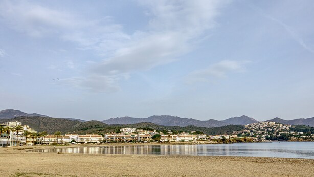 A coastal town with buildings along the shore, a body of water, and mountains in the background.