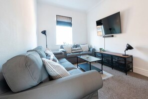 A modern living room with a grey sofa, a coffee table, a TV, and a bookshelf. - Riverside Rest - quirky split-level 3-bed cottage (Ollerton, Nottinghamshire)