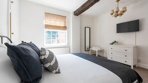Une chambre à coucher avec un grand lit, une table de chevet, un miroir, une commode et un téléviseur fixé au mur.