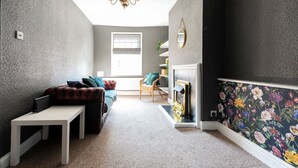 Un salon chaleureux avec une cheminée, un canapé, une petite table et un fauteuil.