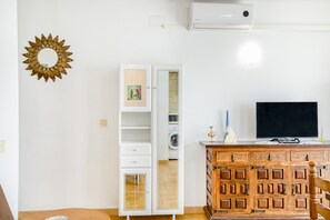 A room with a white wardrobe, a wooden cabinet with decorative panels, a television, and a wall-mounted air conditioner.