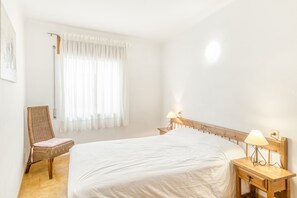 Ein Schlafzimmer mit einem großen Bett, einem Sessel, einem Nachttisch und einem Fenster mit Vorhängen.