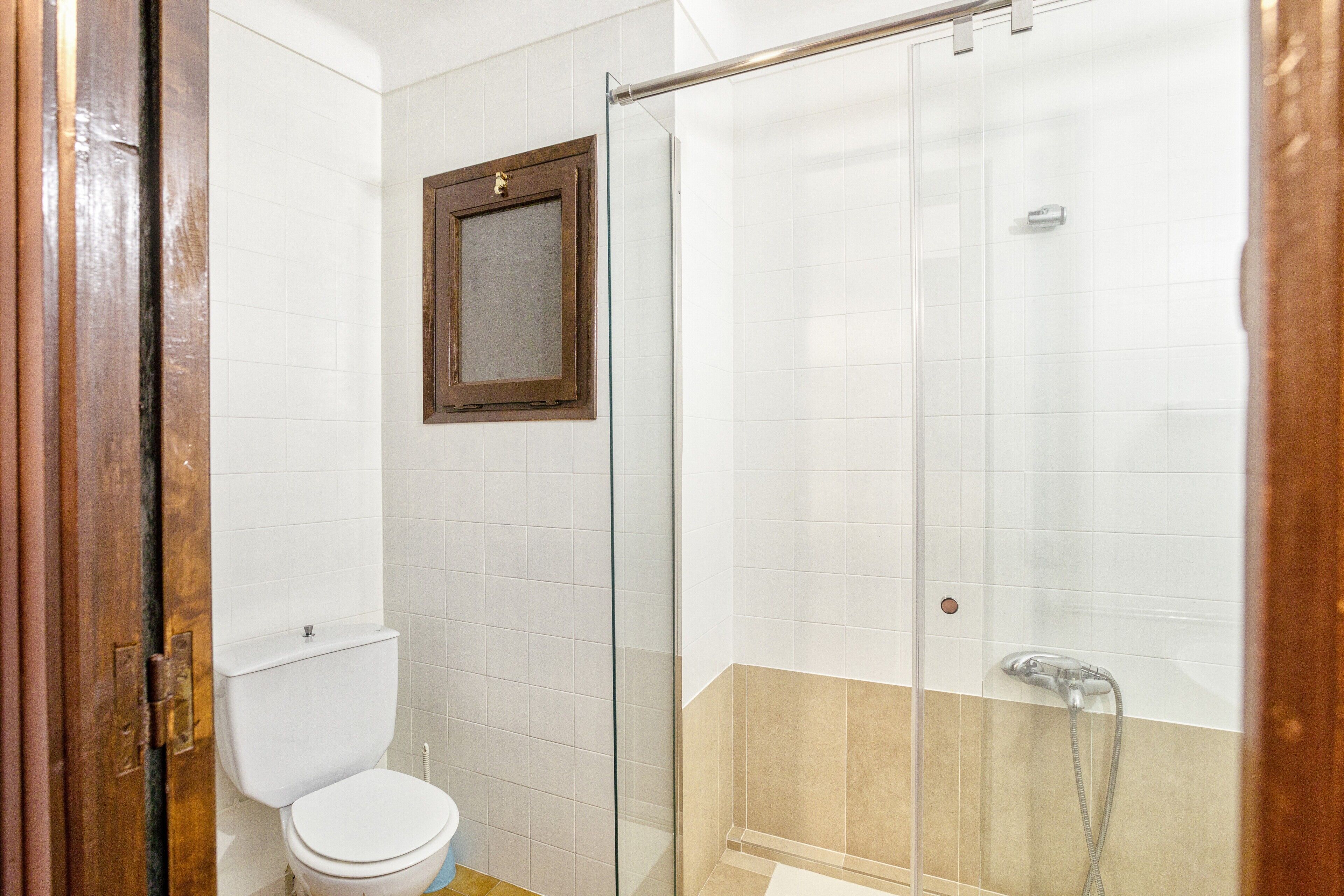 A bathroom with a toilet, a glass shower enclosure, and a wooden door.