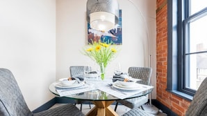 Un coin repas avec une table en verre, des chaises à revêtement gris, un vase avec des fleurs jaunes et un luminaire suspendu moderne.