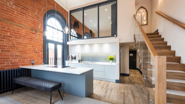Une cuisine moderne dotée d’un grand îlot central, d’un banc et d’un escalier menant à un niveau supérieur.