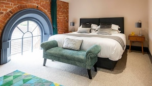 Une chambre à coucher avec un grand lit, un fauteuil vert, un mur en briques et une fenêtre donnant sur un beau paysage.