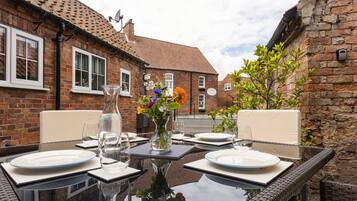 An outdoor dining area with a glass table, white plates, and a vase of flowers.
