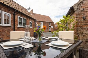 An outdoor dining area with a glass table, white plates, and a vase of flowers. - Ropemaker's Cottage, · Ropemaker's Cottage, cosy cottage retreat (Ollerton, Nottinghamshire)