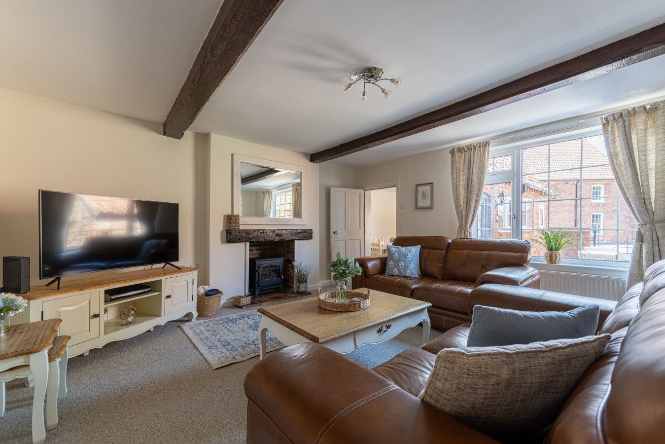 A living room with a flat-screen TV, leather sofas, a fireplace, and a large window with curtains.