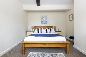 A bedroom with a wooden bed, a blue and white striped pillow, a white duvet, and a gray rug.