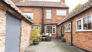 A brick building with a tiled roof, a grey door, and a small patio area with outdoor furniture. - Ropemaker's Cottage, · Ropemaker's Cottage, cosy cottage retreat (Ollerton, Nottinghamshire)