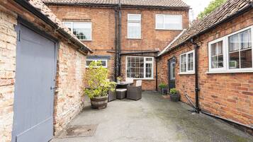 A brick building with a tiled roof, a grey door, and a small patio area with outdoor furniture.