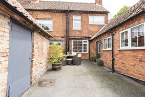 A brick building with a tiled roof, a grey door, and a small patio area with outdoor furniture. - Ropemaker's Cottage, · Ropemaker's Cottage, cosy cottage retreat (Ollerton, Nottinghamshire)