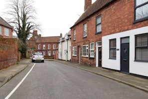 A quiet residential street with brick houses, a white car parked on the side, and a clear road.