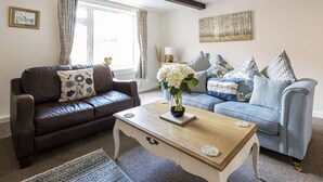 A living room with a brown leather sofa, a blue sofa with patterned cushions, and a wooden coffee table with a vase of flowers. - Ropemaker's Cottage, · Ropemaker's Cottage, cosy cottage retreat (Ollerton, Nottinghamshire)
