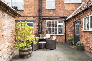 A brick building with a small patio area featuring wicker furniture and potted plants. - Ropemaker's Cottage, · Ropemaker's Cottage, cosy cottage retreat (Ollerton, Nottinghamshire)