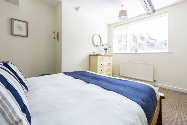 A bedroom with a bed, a dresser, a window, and a radiator.