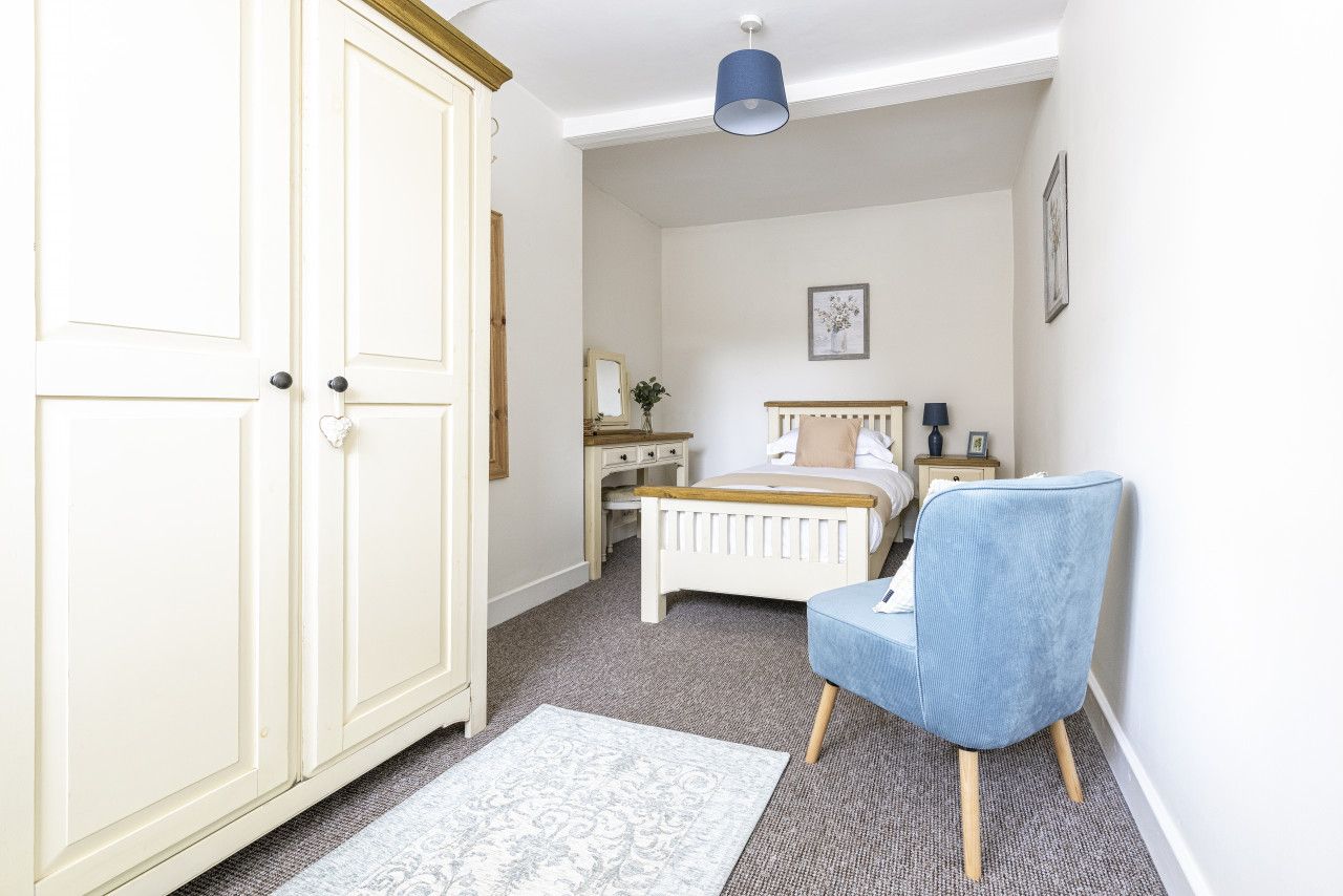 A bedroom with a bed, a chair, a desk, and a wardrobe.