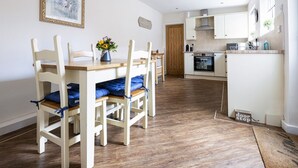 A dining area with wooden chairs and a table, a kitchen with white cabinets, and a wooden floor. - Ropemaker's Cottage, · Ropemaker's Cottage, cosy cottage retreat (Ollerton, Nottinghamshire)