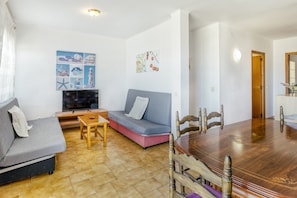 Un salon comprenant un canapé, un téléviseur, une table à manger et une chaise en bois.