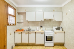 A compact kitchen with white cabinets, a microwave, a stove, and a sink.