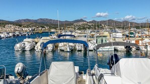 Un puerto deportivo con barcos amarrados, cielo despejado y montañas al fondo.