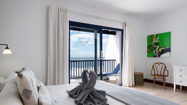 A hotel room with a bed, a chair, a dresser, and a painting on the wall. - Villa 'Malvasia 22' with Sea View, Heated Pool, Balcony, A/C & Wi-Fi (Puerto Calero)