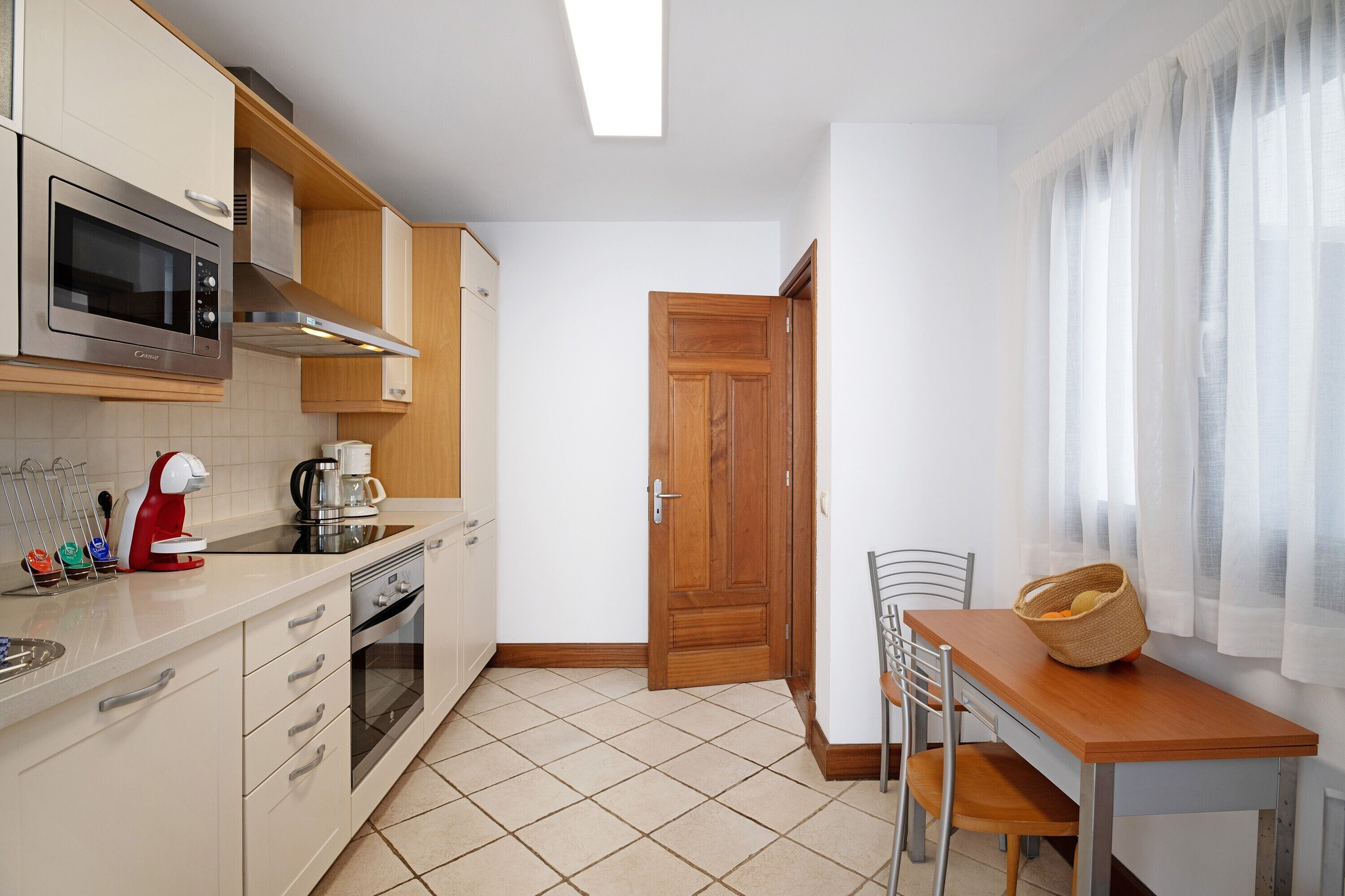 Una cocina con microondas, cafetera y una mesa de comedor con sillas.