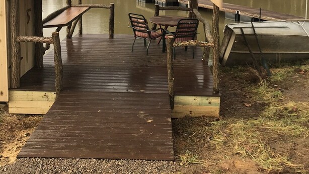 Eine Holzsteganlage mit überdachter Sitzgruppe und Tisch, mit Blick auf ein Gewässer.