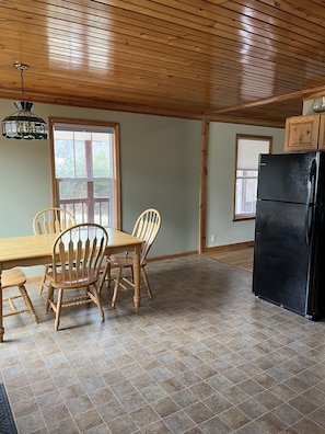 A kitchen with wooden cabinets, a black refrigerator, a dining table with chairs, and a window with blinds.