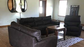 Ein geräumiges Wohnzimmer mit einem großen Ecksofa, einem passenden Sessel und einem Holztisch.