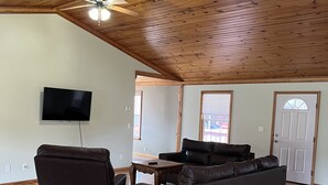 Ein geräumiges Wohnzimmer mit Holzbalkendecke, einem wandmontierten Flachbildfernseher, einem Ledersofa und einem Couchtisch.