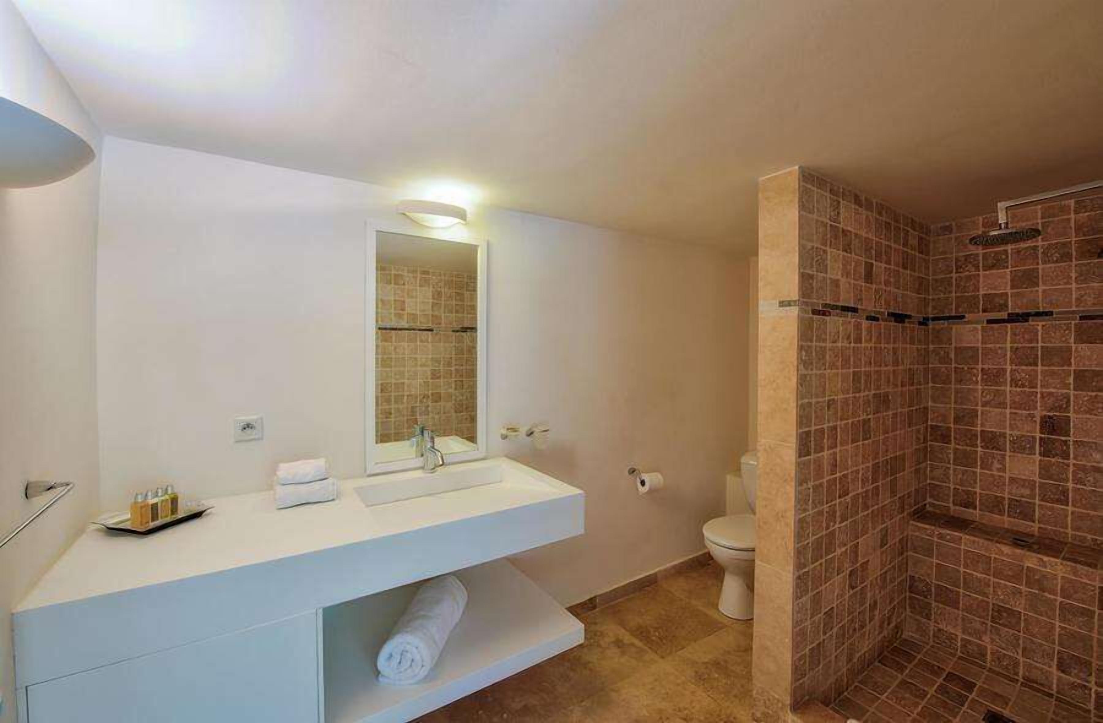 Un baño moderno con un tocador blanco, un espejo grande, un inodoro y una zona de ducha con paredes de azulejos.