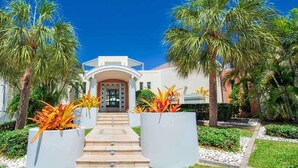 A hotel entrance with a central staircase, palm trees, and a white building facade. - Les Palmiers Bleus Luxury villa (Les Terres Basses)