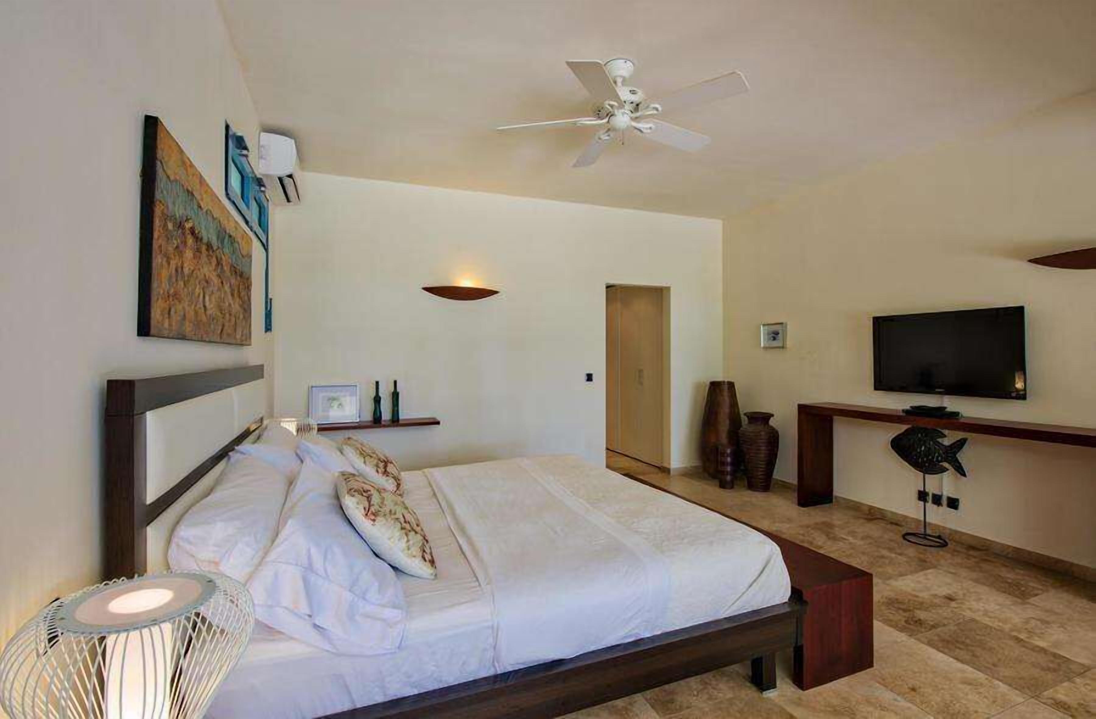 A bedroom with a bed, bedside table, TV, and artwork on the wall.
