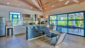 A modern kitchen with a glass dining area, large windows, and a ceiling fan. - Les Palmiers Bleus Luxury villa (Les Terres Basses)