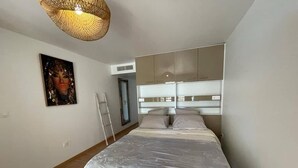 Un dormitorio con cama, cabecera, escalera, un cuadro y una lámpara en el techo.