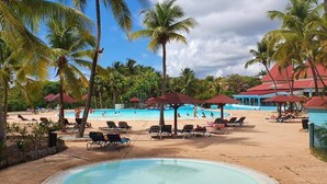 Un área de piscina con sillones de descanso y sombrillas, rodeada de palmeras y una playa.