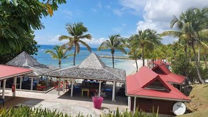 Un resort frente a la playa con un área de estar techada, palmeras y vistas al océano.