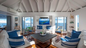 A spacious living room with a large TV, comfortable seating, and a view of the sea. - Cap Au Vent (2/4 Rooms) (Pointe Milou)